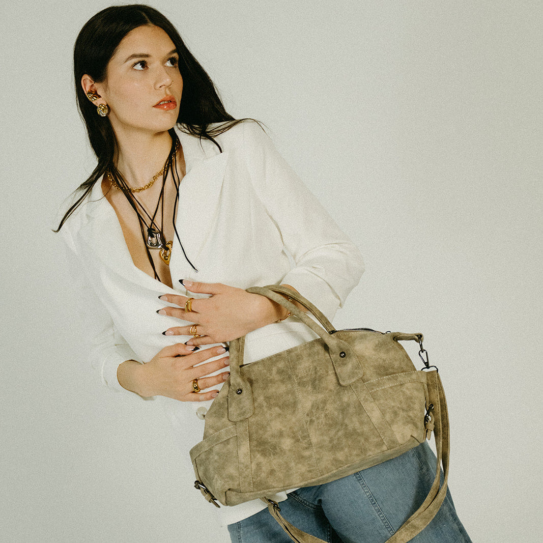 Woman holding a beige handbag against a plain background