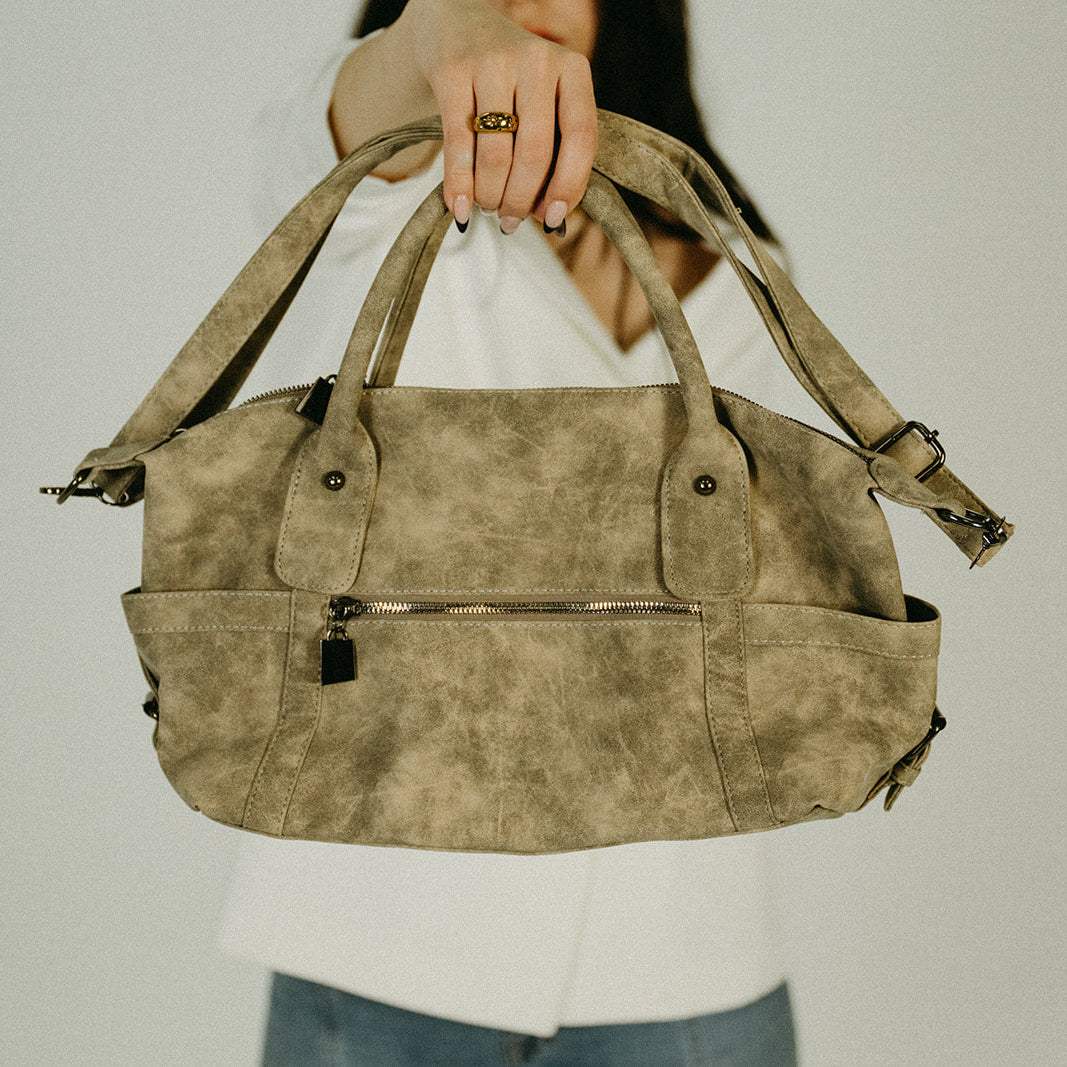 Person holding a brown leather handbag against a plain background