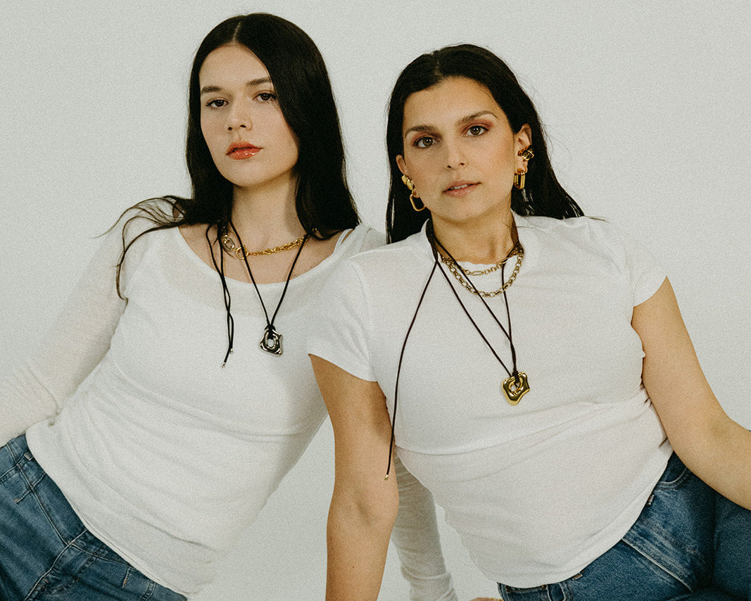 Two women sitting on a white floor wearing white tops and blue jeans.