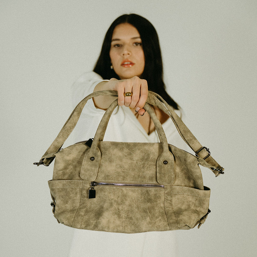 Woman holding a green suede bag against a plain background