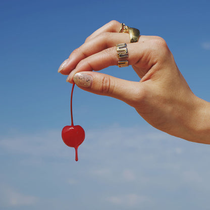 Hand holding a red cherry against a blue sky